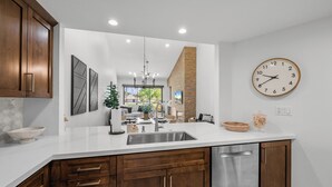 A modern kitchen with wooden cabinets, a stainless steel sink, and a wall clock. - 3 Bedroom Luxury Condo on Fairway at Palm Valley CC! Available January 2027! (Palm Desert)