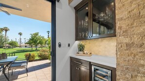 A kitchen with a view of a golf course, a dining area with outdoor seating, and a brick wall. - 3 Bedroom Luxury Condo on Fairway at Palm Valley CC! Available January 2027! (Palm Desert)