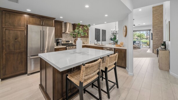 A modern kitchen with wooden cabinets, a stainless steel refrigerator, and a large island with bar stools. - 3 Bedroom Luxury Condo on Fairway at Palm Valley CC! Available January 2027! (Palm Desert)