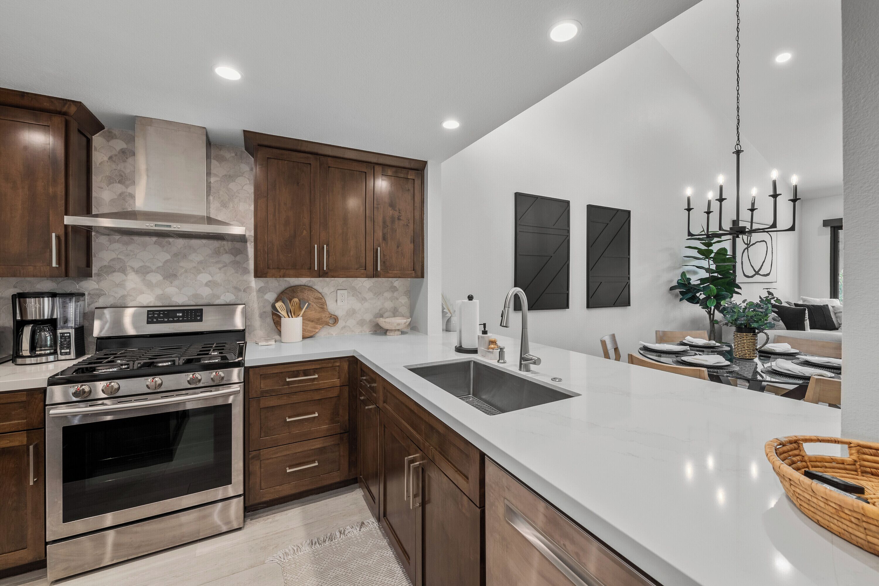 A modern kitchen with wooden cabinets, stainless steel appliances, a large island with a sink, and a chandelier.