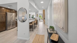 A modern kitchen with stainless steel appliances, a dining area with bar stools, and a large abstract painting on the wall. - 3 Bedroom Luxury Condo on Fairway at Palm Valley CC! Available January 2027! (Palm Desert)