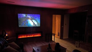 Ein gemütliches Wohnzimmer mit einem wandmontierten Flachbildfernseher, einem Kamin mit Feuer, einem Ledersofa und einem Couchtisch.