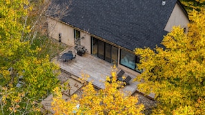 A modern house with a deck, large windows, and a view of surrounding trees. - Original Cabin (Lac-Supérieur)