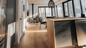 A modern kitchen with wooden flooring, a central island, and large windows. - Cabine Origine  (Lac-Supérieur)