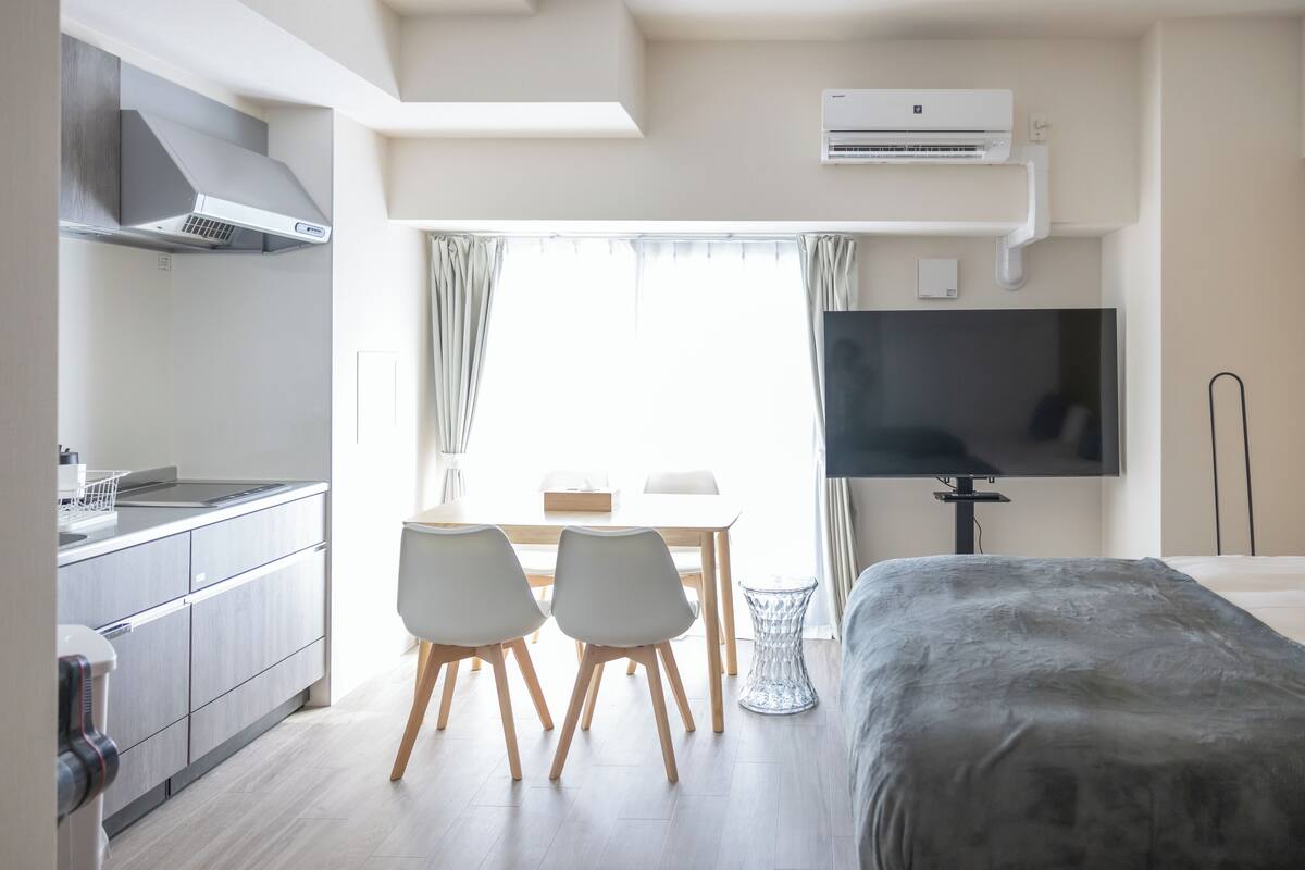 Une chambre d’hôtel moderne dotée d’une kitchenette, d’un coin repas avec deux chaises, d’un lit et d’un téléviseur à écran plat fixé au mur.