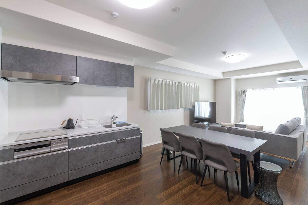 Une cuisine moderne avec des meubles gris, un four encastré et un coin repas comprenant une table et des chaises.