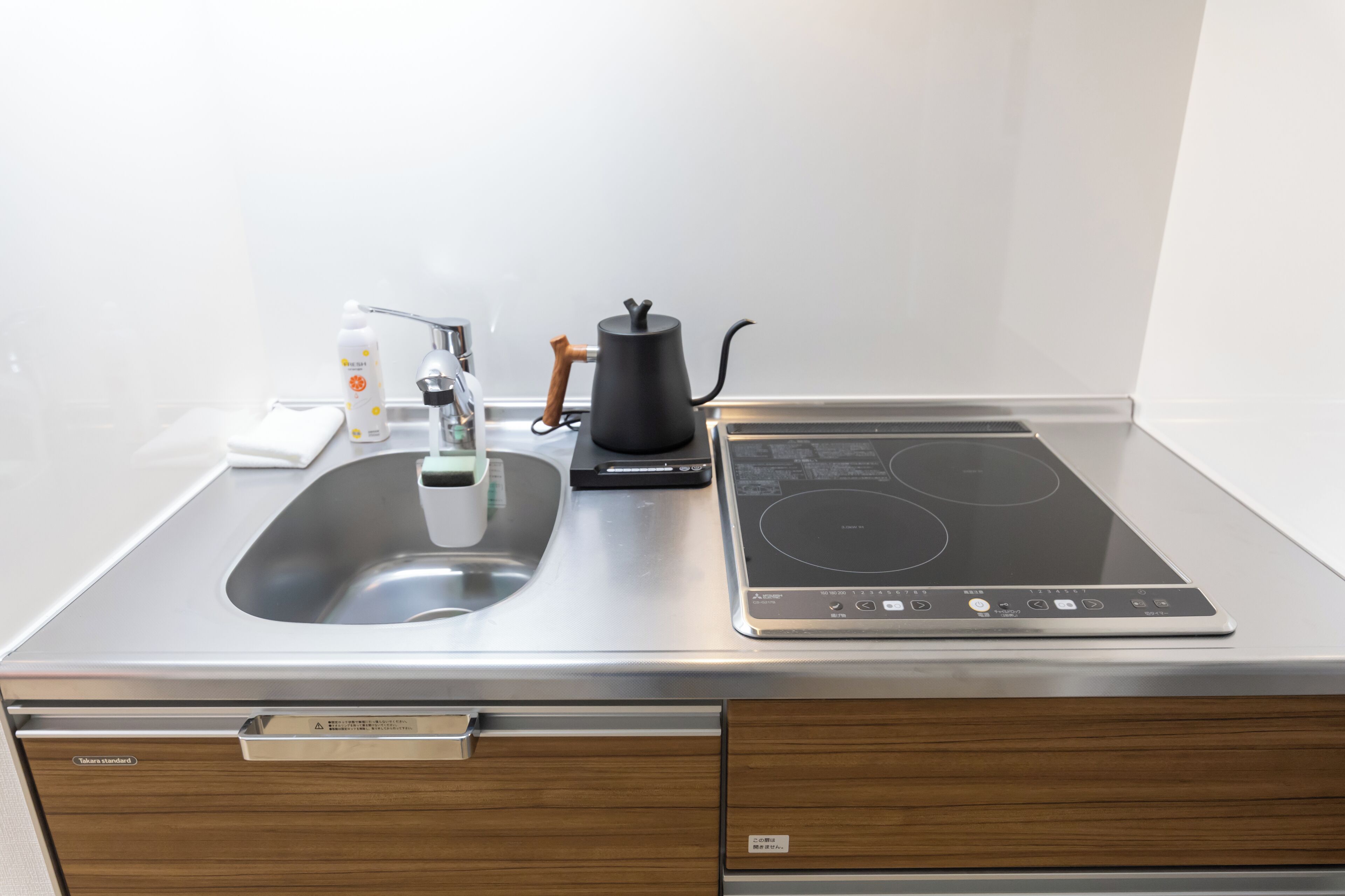 A modern kitchen with a stainless steel sink, a black kettle, and a built-in induction cooktop.