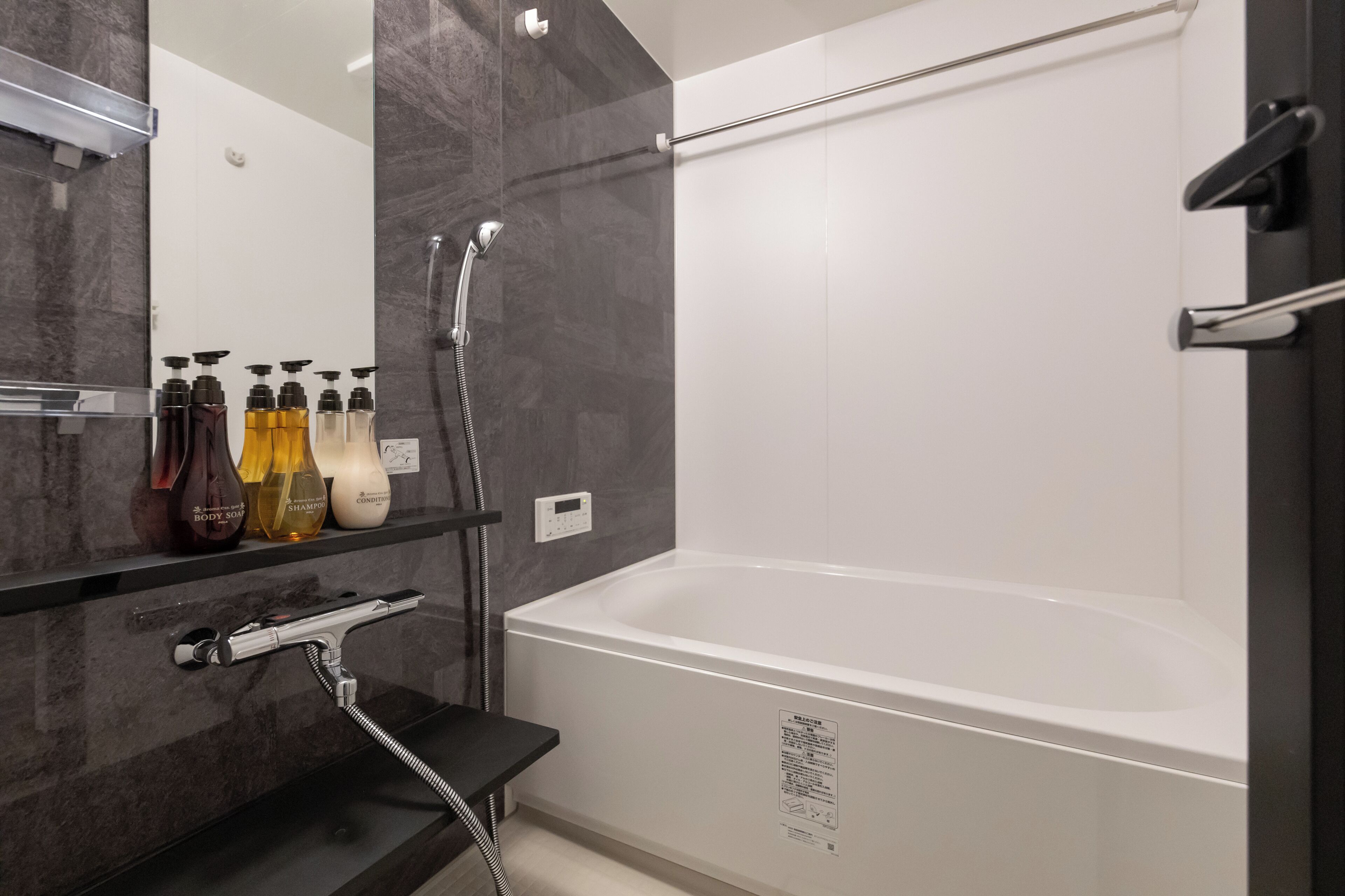 Een moderne badkamer met een groot bad, een douche en een wastafel met zeepdispensers.
