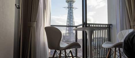 A balcony with two chairs and a table, overlooking a tower with Japanese text.