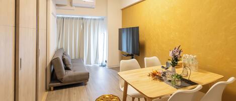 A modern living room with a sofa, a dining table with chairs, and a TV mounted on the wall.