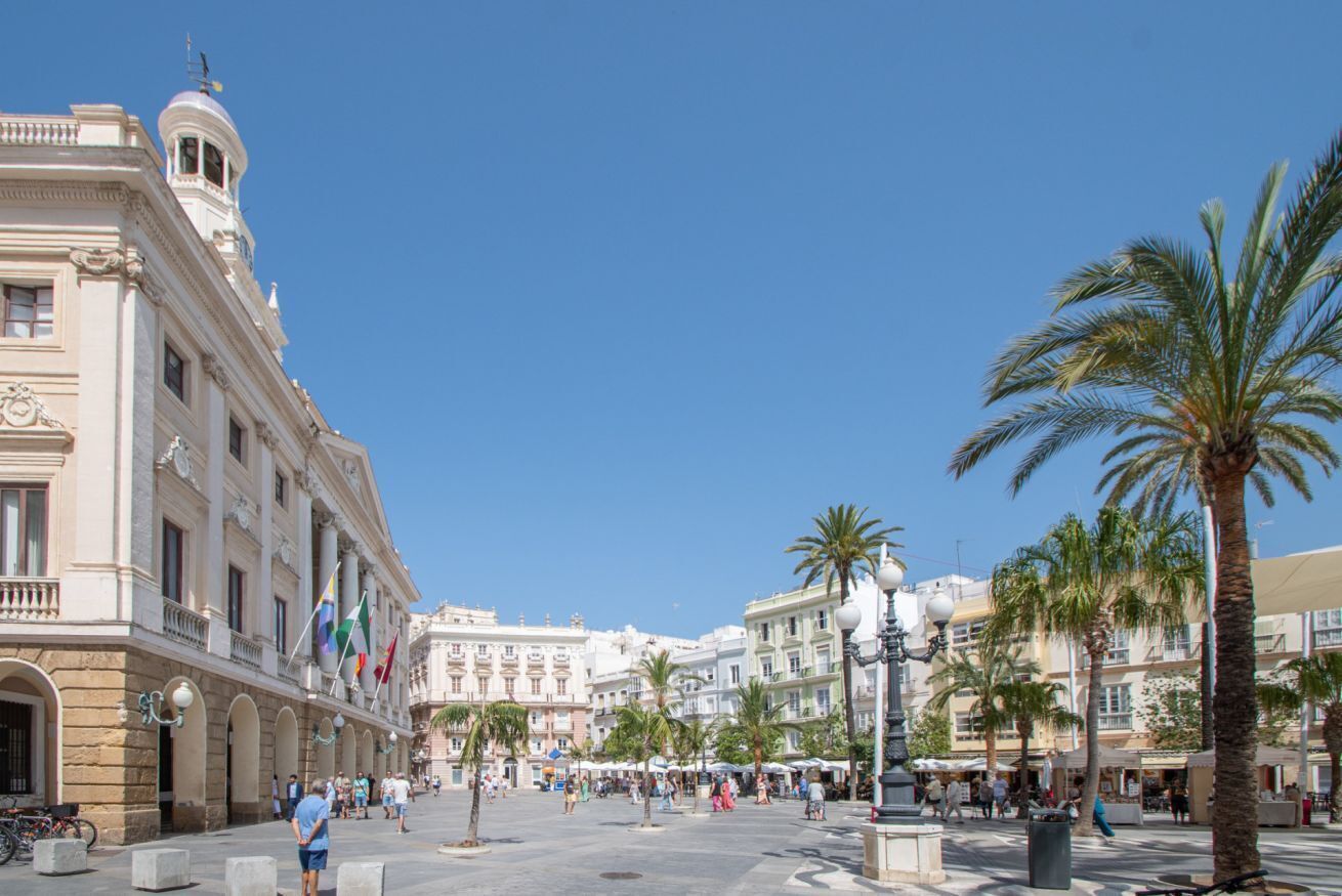 A public square with historical buildings, palm trees, and outdoor seating areas.