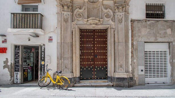 Ein Gebäude mit einer großen, verzierten Holztür, einem Fahrrad davor und einem Schild, das auf das offene Geschäft hinweist.