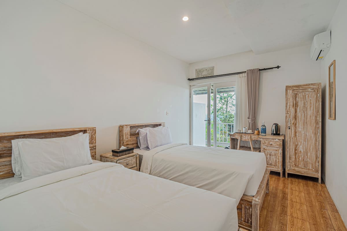 Een slaapkamer met twee bedden, een houten garderobe, een kleine tafel met een waterkoker en een raam met gordijnen.