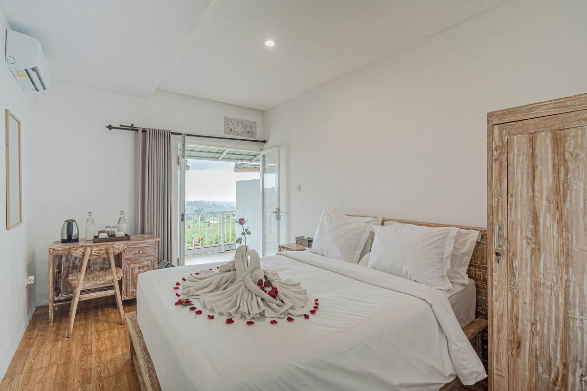Een slaapkamer met een bed, een bureau en een stoel. Er is een balkon met uitzicht op het omliggende landschap.
