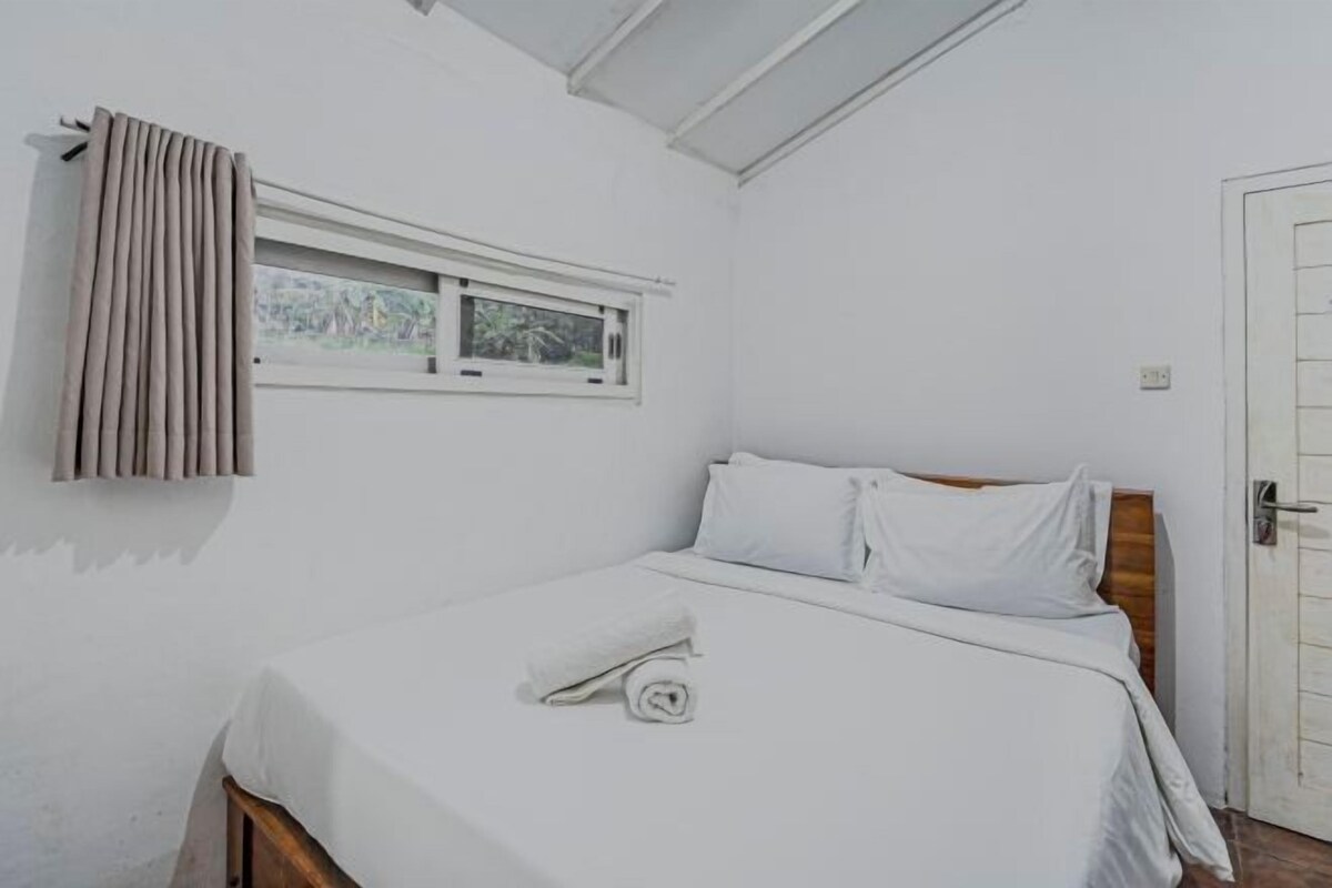 Une chambre avec un lit simple, une tête de lit en bois, une fenêtre avec des rideaux et une porte blanche.