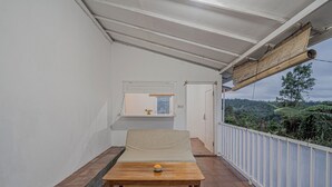 A balcony with a wooden table, a beige sofa, and a view of a lush landscape. - Santya Loka Lodge & Twin Waterfall (Penebel)