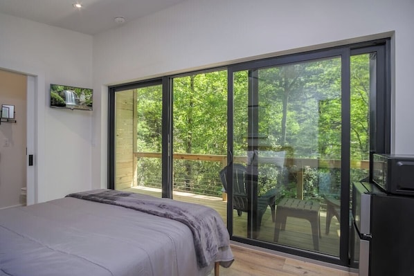 Un dormitorio con un gran ventanal corredera que da a un balcón con vistas a árboles.