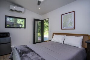 Un dormitorio con cama, escritorio, aire acondicionado, ventana y puerta que da a un espacio exterior.