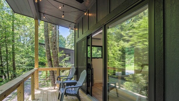 Eine Holzdar Terrasse mit Stühlen, einer Glastür und Blick auf einen Wald.