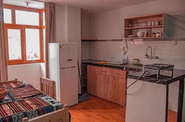 A compact kitchen with a refrigerator, wooden cabinets, a sink, and a window with curtains. - Mountain view mini-apartment (Chivay)