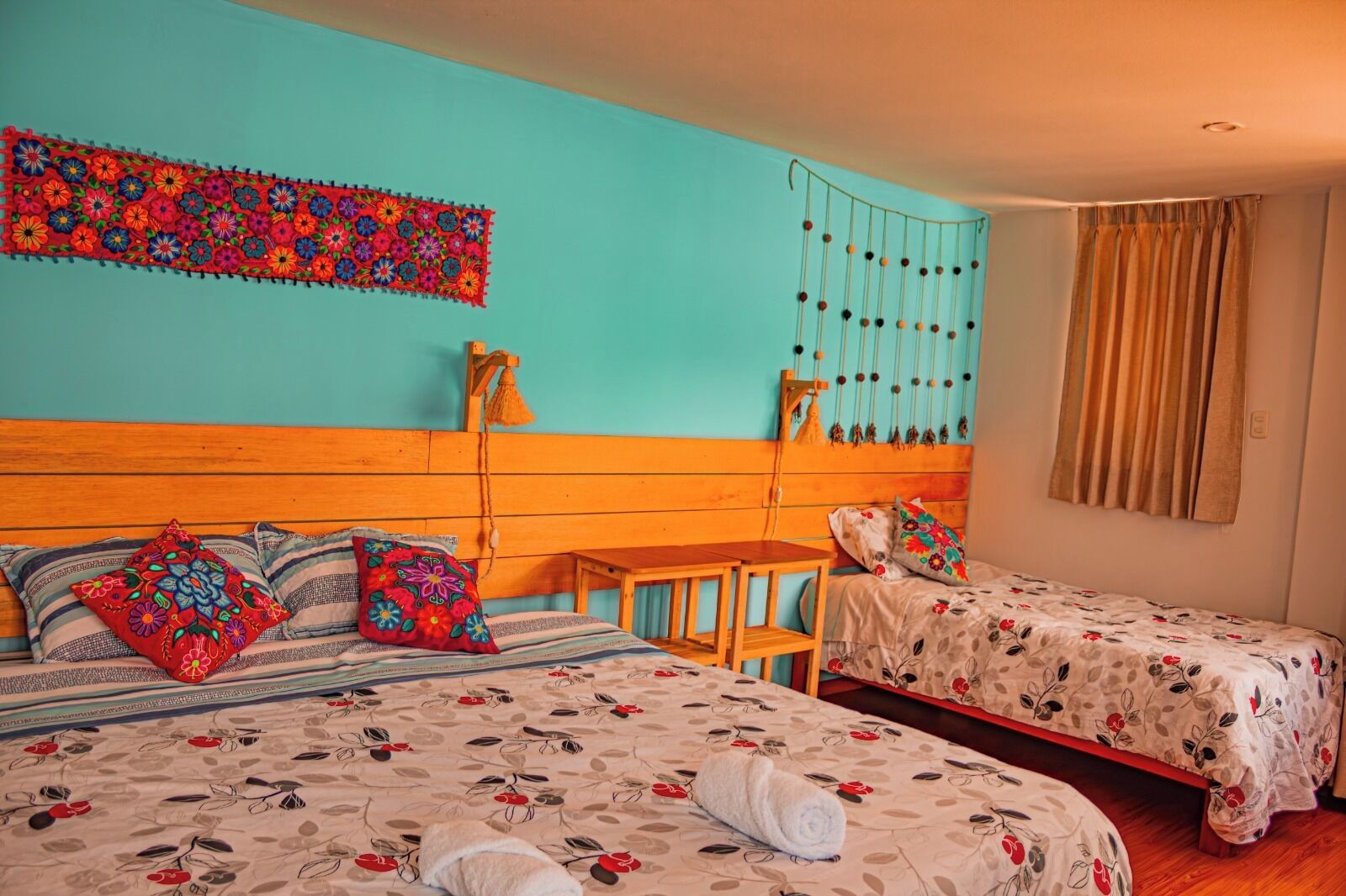 Une chambre avec deux lits, une tête de lit en bois, une décoration murale, un luminaire suspendu et une fenêtre avec des rideaux.