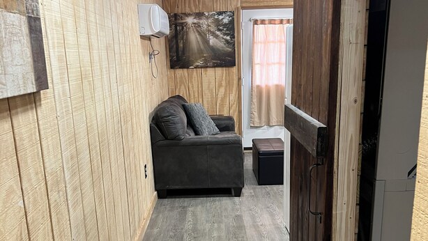 A narrow hallway with wooden walls and a grey floor, leading to a room with a sofa and a painting. - Cozy cabin in charming Ponca City with WiFi, AC (Ponca City)
