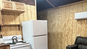 A compact kitchen with wooden cabinets, a white refrigerator, a stove, and a black sofa. - Cozy cabin in charming Ponca City with WiFi, AC (Ponca City)