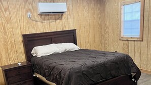 A bedroom with a wooden bed frame, a nightstand, and a wall-mounted air conditioning unit. - Cozy cabin in charming Ponca City with WiFi, AC (Ponca City)