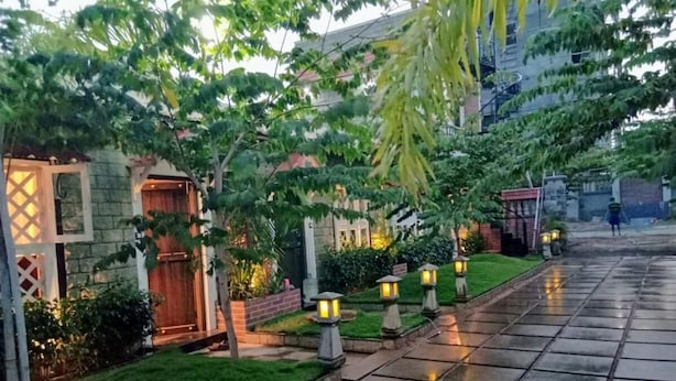 A pathway lined with evenly spaced lanterns, leading to a building with a wooden door and a stone wall. - FERDIN COTTAGE (Nagercoil)