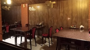 A restaurant with a long wooden table and red chairs, a brick wall, and a wooden ceiling. - FERDIN COTTAGE (Nagercoil)