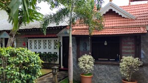 A residential building with a red-tiled roof, a stone facade, and a white lattice front door. - FERDIN COTTAGE (Nagercoil)