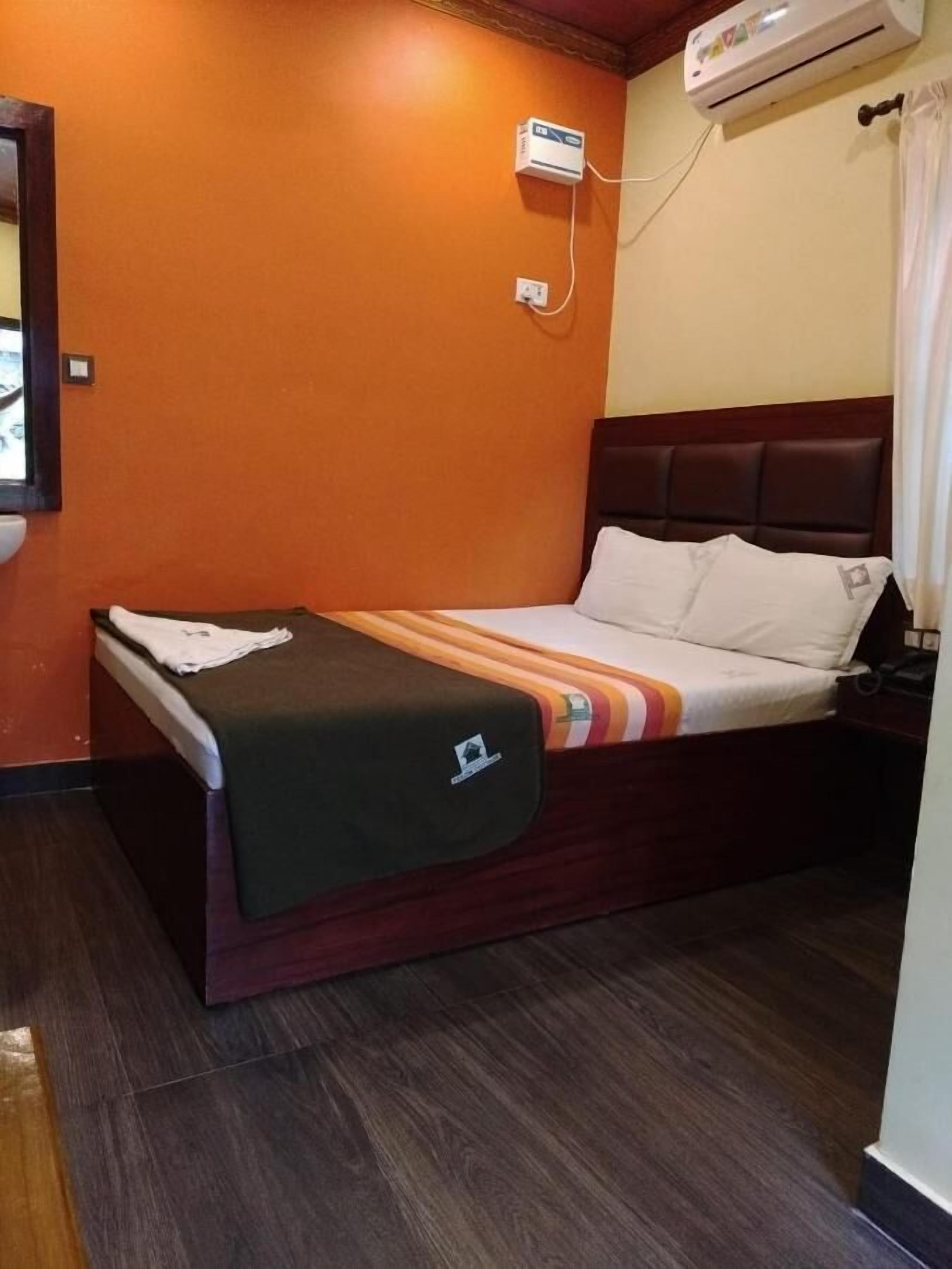 A single bed with a dark headboard, a bedside table, and an air conditioning unit mounted on the wall.