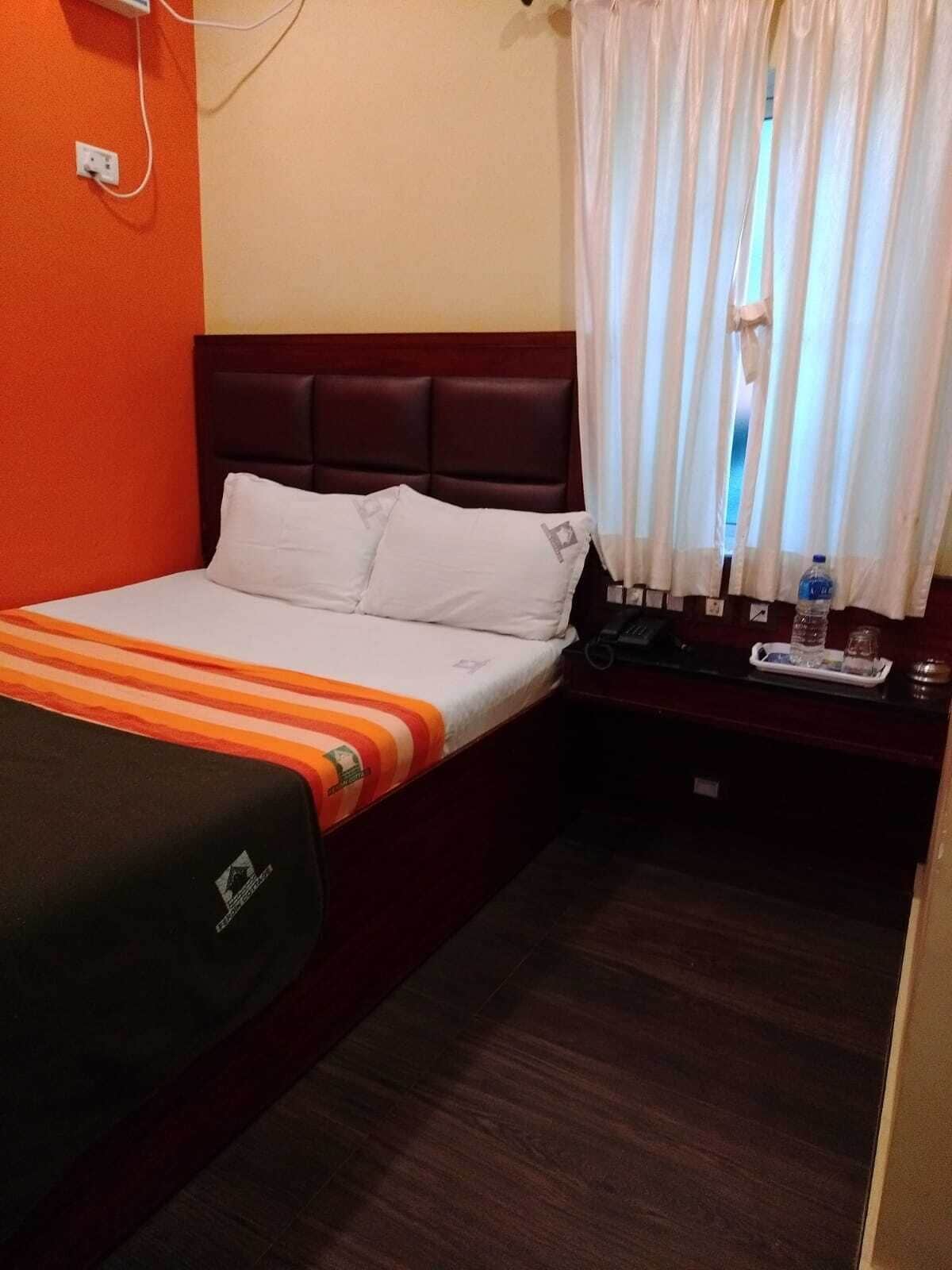 Una camera d'albergo con un letto, un comodino, una bottiglia d'acqua e una finestra con tende.