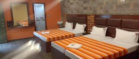 Quarto de hotel com duas camas, cada uma com roupa de cama e almofadas listradas, um painel de cabeceira com padrão de tijolos e um aparelho de ar condicionado na parede.