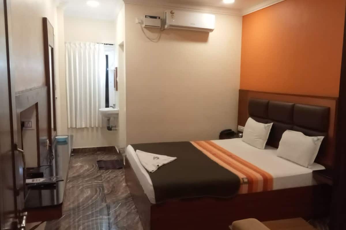 A hotel room with a bed, a bedside table, a mirror, a sink, and an air conditioning unit.