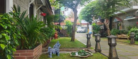 Ein Garten mit einer Statue, einem kleinen Teich und einem Auto auf der Straße.