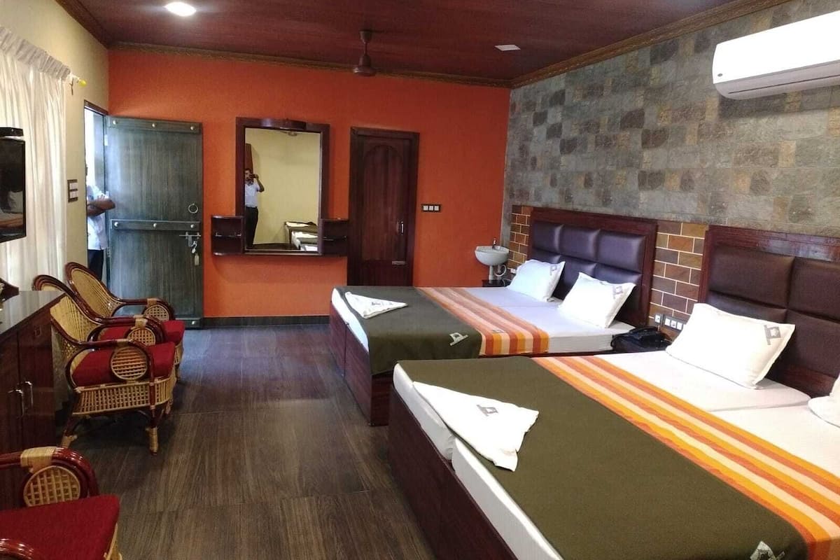 A hotel room with two beds, a sitting area with chairs, a mirror, and a stone wall.