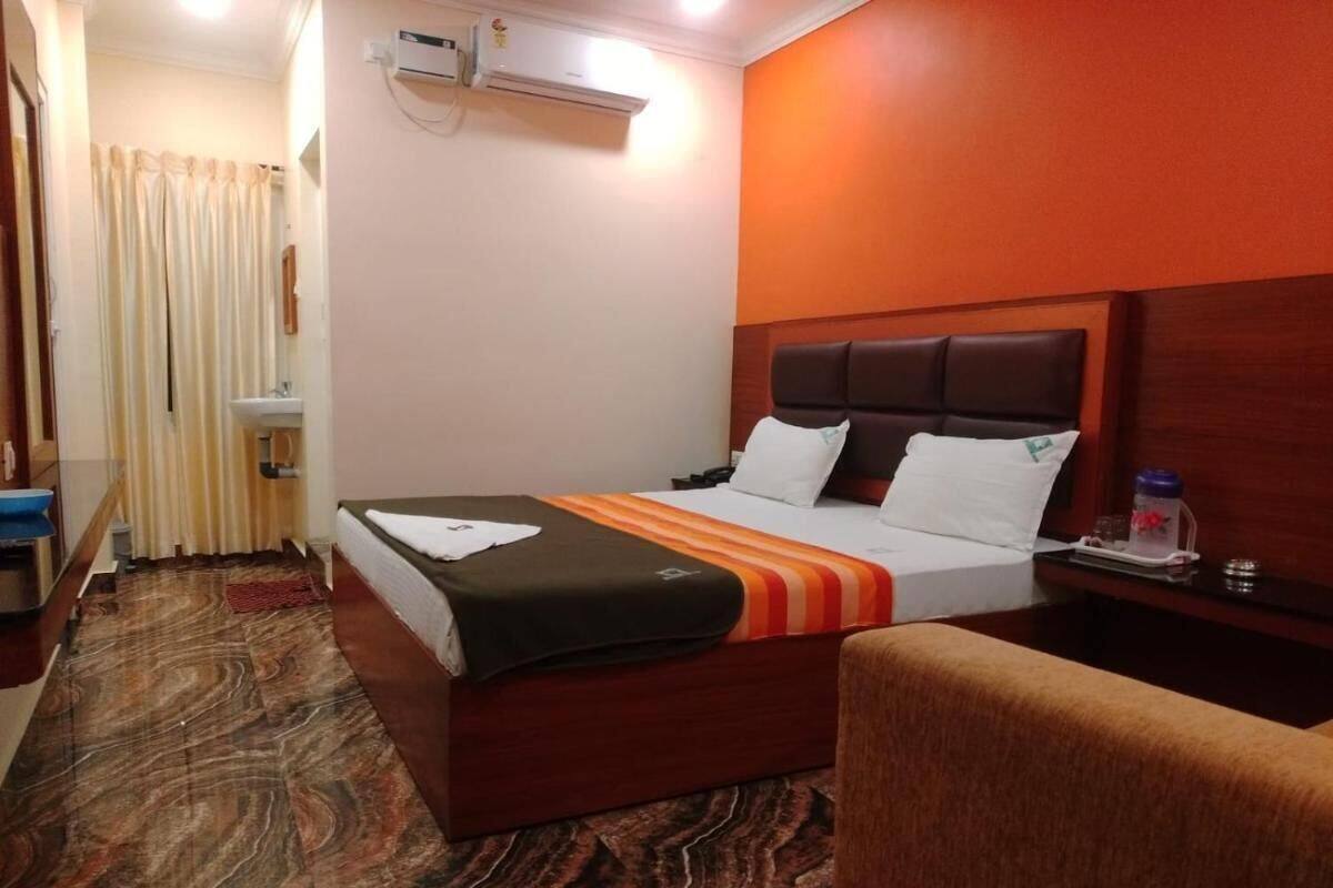 A hotel room with a bed, a bedside table, a chair, a bathroom with a shower curtain, and an air conditioning unit.