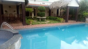 A swimming pool with a tiled deck, surrounded by chairs and potted plants. - FERDIN COTTAGE (Nagercoil)