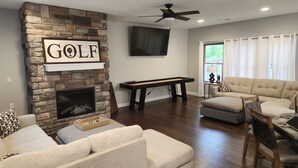 A living room with a stone fireplace, a flat-screen TV, a ceiling fan, a billiards table, and a beige sofa. - 3-bedroom house located near Camdenton. Nestled In Old Kinderhook community.  (Camdenton)