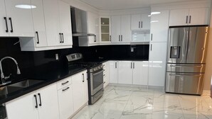 Een moderne keuken met witte kastjes, een zwart aanrechtblad, roestvrijstalen apparatuur en een marmeren vloer.