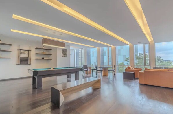 A spacious room with a pool table, comfortable seating, and large windows offering a view of the outdoors.
