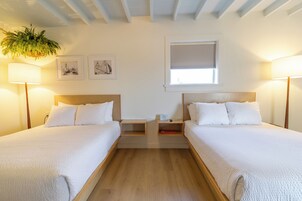 Habitación doble con dos camas, cabeceros de madera, mesitas de noche, una planta colgante y cuadros en la pared.