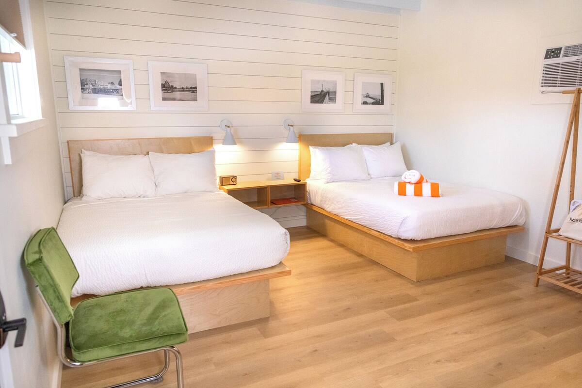 A double room with two beds, wooden headboards, bedside tables with lamps, and framed pictures on the wall.