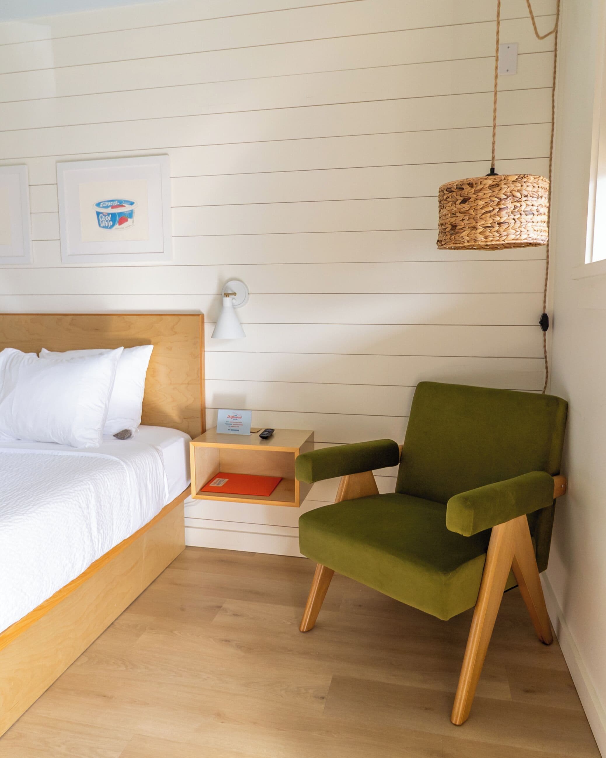 A bedroom with a wooden bed, a green chair, a bedside table with a lamp, and a woven light fixture.