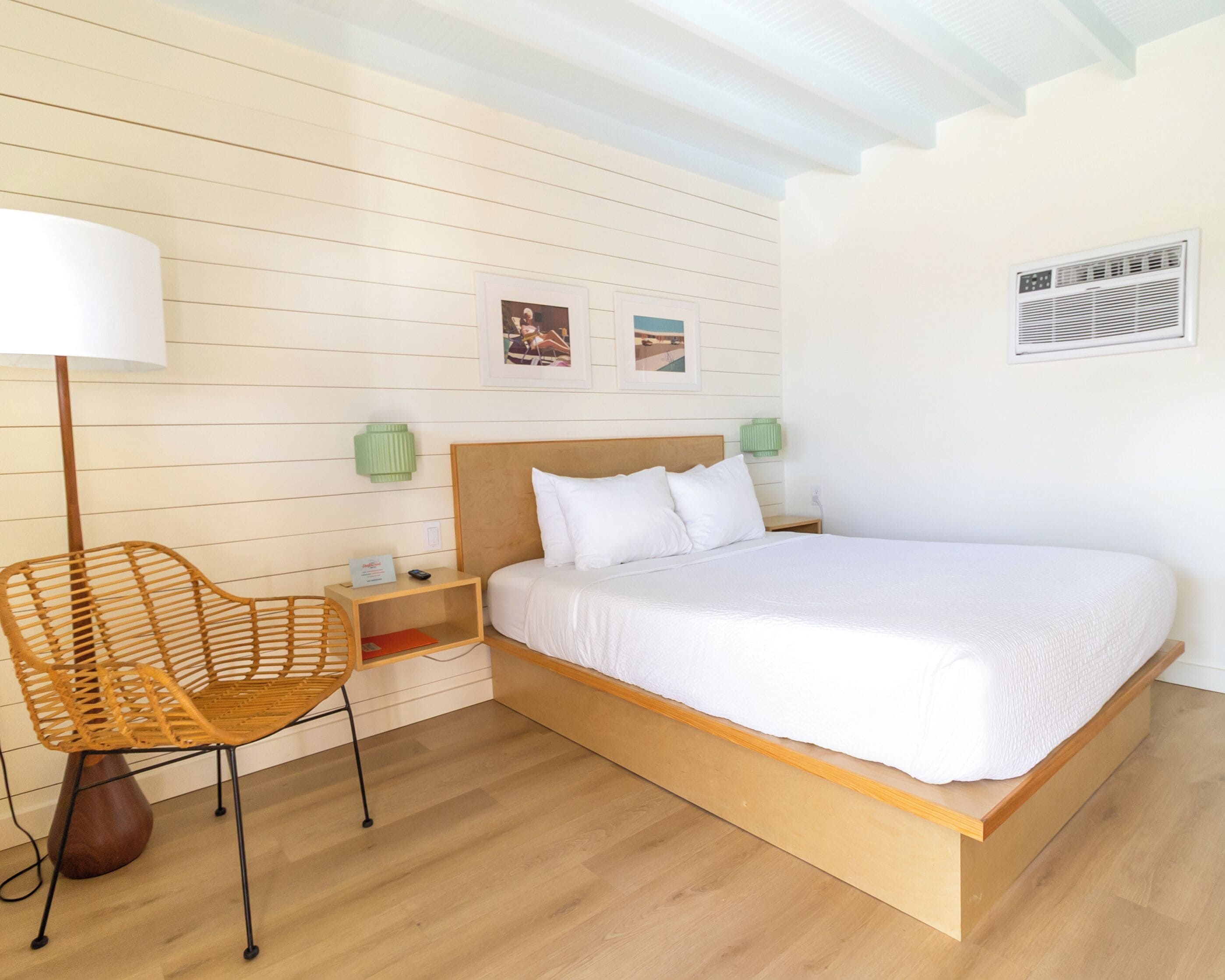 Ein Schlafzimmer mit einem hölzernen Bett, einem Korbstuhl, einem Nachttisch und einer Wand-Klimaanlage.