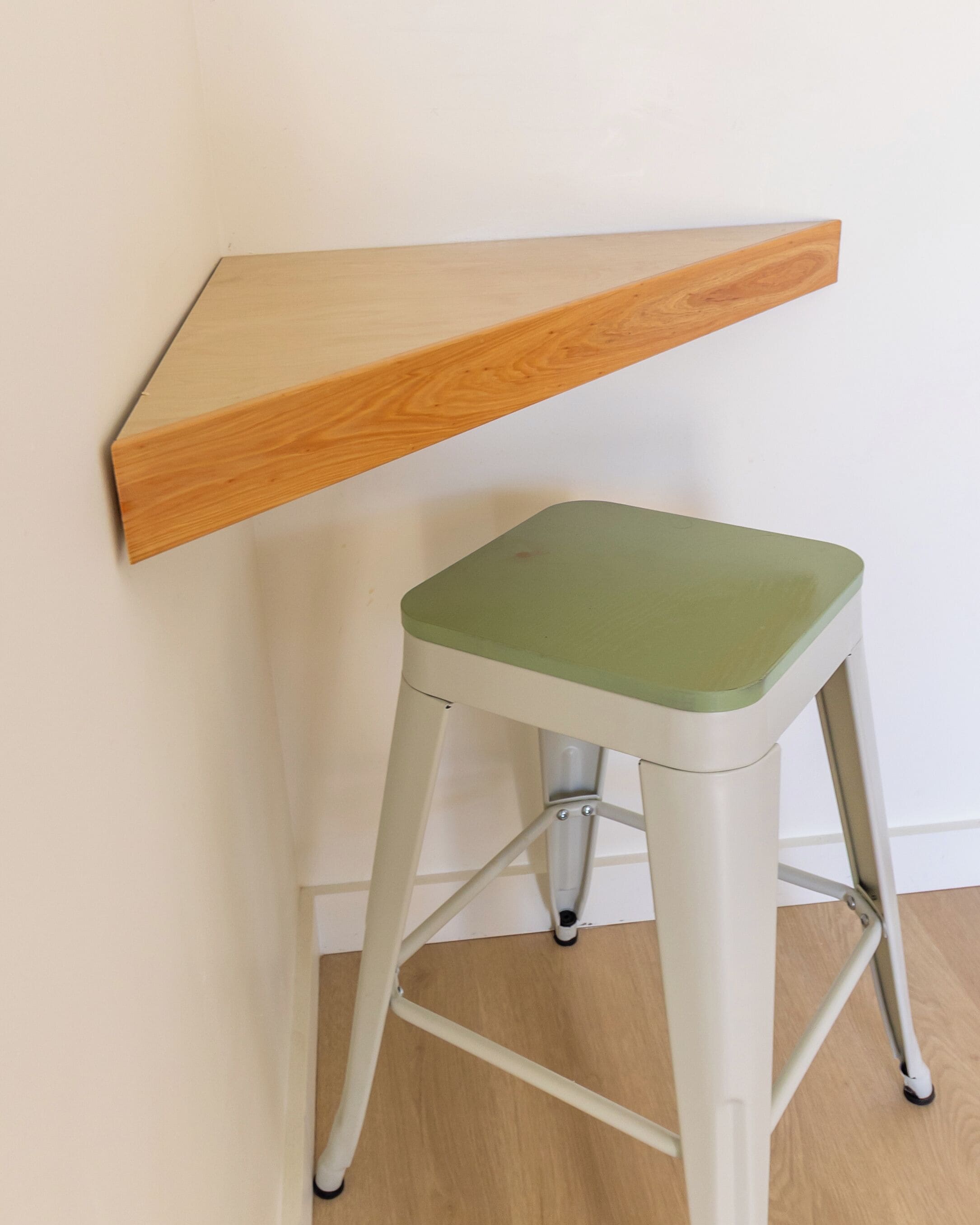 A stool with a green seat and a wooden shelf attached to a white wall.