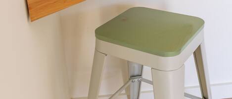 A stool with a green seat and a wooden shelf attached to a white wall.