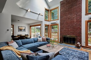A spacious living room with a large blue sectional sofa, a fireplace, and multiple windows providing natural light.