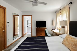 A hotel room with a bed, a television, a desk with a lamp, and a chair.